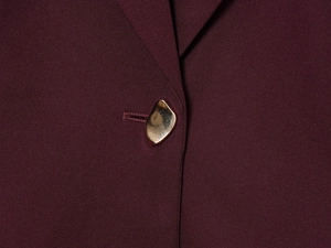 Close-up of a burgundy blazer featuring a unique irregular gold metal button detail