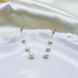 Détail de boucles d'oreilles perles baroques et chaînes dorées sur plateau céramique