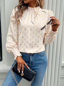 Detail of white long sleeve blouse featuring golden polka dots and ruffled elastic cuffs