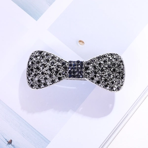 Détail d'une pince à cheveux vintage avec strass noirs et bleus en forme de nœud