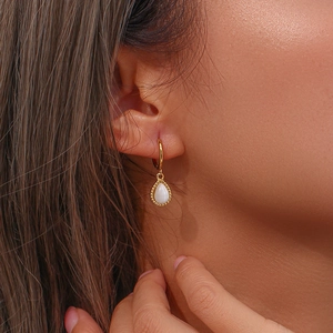 Close-up of golden teardrop earrings with white stone and beaded edge on a model