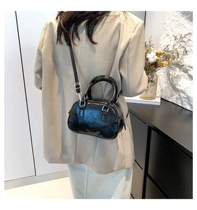 Detail view of a black glossy leather mini bowling bag worn by a model in a beige suit