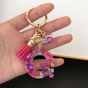 Detail of resin letter G keychain with pink tassel, colorful stones, and star glitter ball