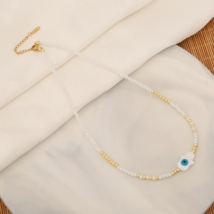 Beaded Hamsa necklace with evil eye pendant on white marble and draped fabric background