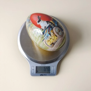 Detailed scale view showing the 64.6g weight of this vintage tin Easter egg storage box