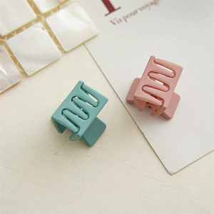 Close-up of matte square mini hair claws in teal and pink on a textured background