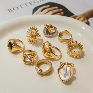 Assortment of luxury gold plated titanium rings with pearls and emerald gems on a white tray