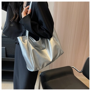 Sac fourre-tout argenté métallisé avec texture plissée porté à l'épaule sur veste noire