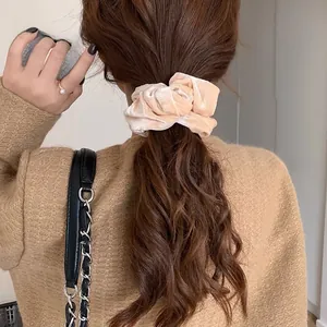 Dettaglio di uno scrunchie in velluto champagne su una coda di cavallo con lucentezza