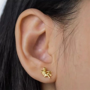 Macro shot of gold angel wing stud earring worn on ear showing delicate craftsmanship