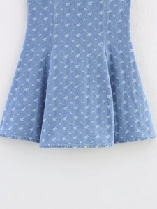 Dettaglio ravvicinato della gonna in denim blu con fiori bianchi e orlo a trapezio