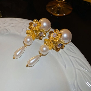Macro view of gold flower earrings with tassels and pearls on a white ceramic plate