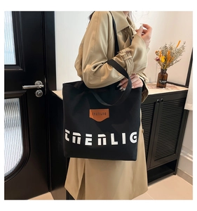 Detail shot of the black canvas tote bag showing the leather logo and white lettering