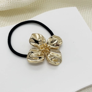 Close-up of a black elastic hair tie featuring a golden metal four-petal flower charm