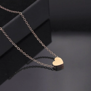 Gros plan du collier avec pendentif cœur en or rose se reflétant sur une surface noire lisse
