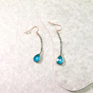 Elegant gold drop earrings with blue crystal teardrops and tassel chain on marble