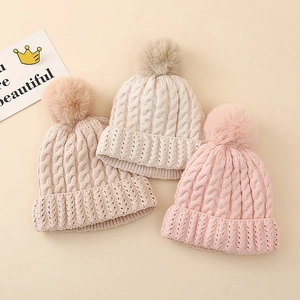 Winter cable-knit baby beanies with faux fur pompoms in cream, beige, and pink colors
