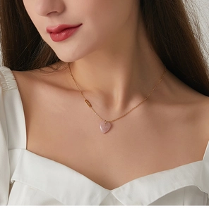 Model wearing gold lucky tag necklace with a heart-shaped pink crystal pendant