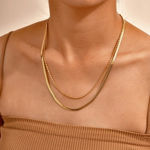 Detail of layered gold snake chain and beaded necklace on neck showing metallic luster