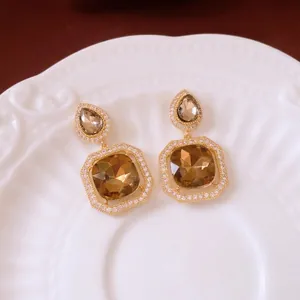 Elegant gold earrings with champagne square zircon and pear drops on white ceramic