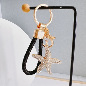 Close-up of golden starfish keychain with rhinestones and black braided leather strap
