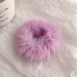 Close-up of soft purple faux fur hair tie scrunchie on textured white background