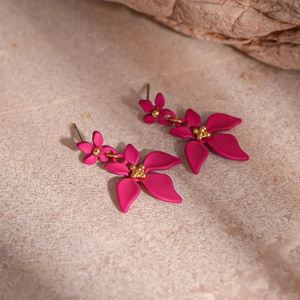 Détail des boucles d'oreilles fleur magenta avec centre doré sur un support en pierre