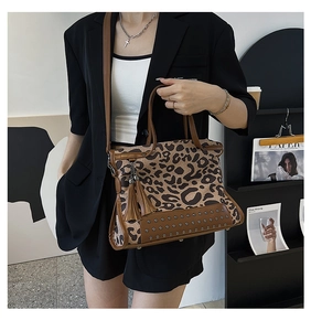 Detail view of leopard print handbag with brown leather trim, metal studs and fringe tassel