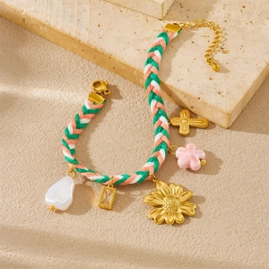 Detailed view of woven bracelets with flower and pearl charms on beige stone