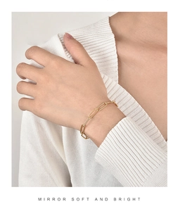 Nahaufnahme eines goldenen Büroklammer-Armbands am Handgelenk vor Strickhintergrund