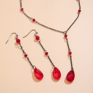 Detail view of red faceted bead necklace and teardrop earrings set on beige background