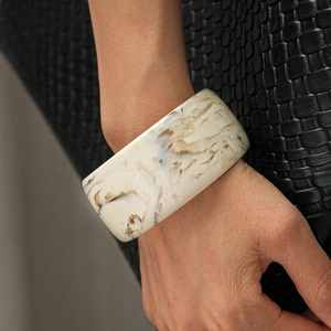 Macro view of wide resin bangle featuring cream marble texture on a black leather background