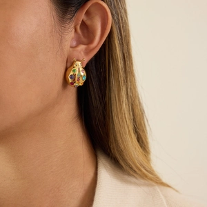 Close-up of a golden ladybug stud earring with multi-colored gemstones on a model's ear