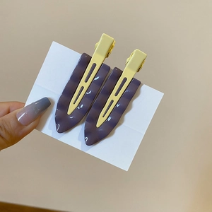 Detail view of two minimalist wavy purple and yellow resin hair clips with duckbill base