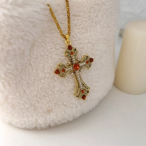 Détail d'un collier croix doré vintage avec pierres rouge rubis sur fond en peluche