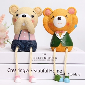 Detailed view of creative resin bear figurines with hanging rope legs on book stack