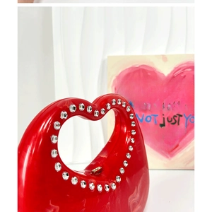 Close-up of a red heart-shaped acrylic handbag with sparkling rhinestone handle detail