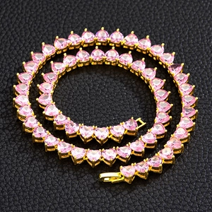 Macro shot of gold tennis chain necklace with pink heart-shaped stones on black texture