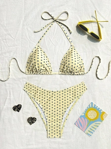 Bikini giallo a pois con top a triangolo e slip a gamba alta su sfondo di tessuto bianco