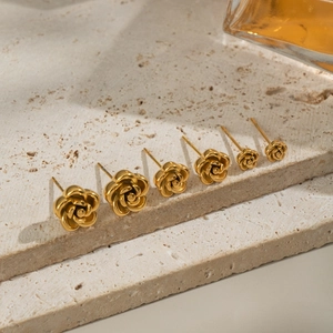 Set of six golden rose stud earrings in various sizes on beige stone background