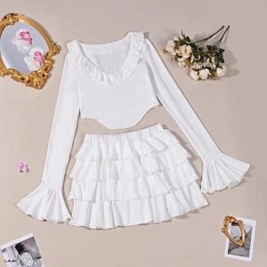 Flat lay di un completo bianco con top corto a balze e minigonna a strati, decoro vintage