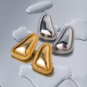 Macro detail of gold and silver waterdrop earrings with textured beaded edges and reflection
