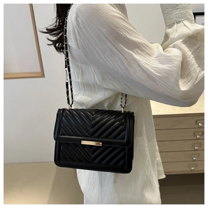 Detail of black quilted shoulder bag with gold chain strap and metal buckle on a model
