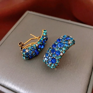 Boucles d'oreilles vintage dorées en C avec cristaux bleus sur un coffret gris