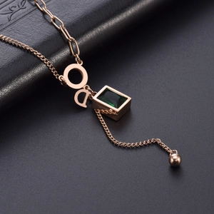 Rose gold necklace featuring emerald green pendant and CD logo on textured leather background