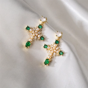 Détail de boucles d'oreilles croix avec gemmes vertes et perles sur soie blanche
