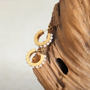 Orecchini a cerchio dorati a forma di C con piccole perle bianche su superficie in legno