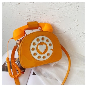 Detail of creative vintage telephone bag in bright orange patent leather with heart dial