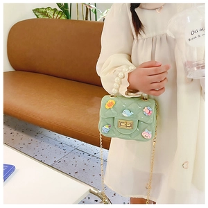 Detail of light green quilted child crossbody bag with pearl handle and cartoon charms