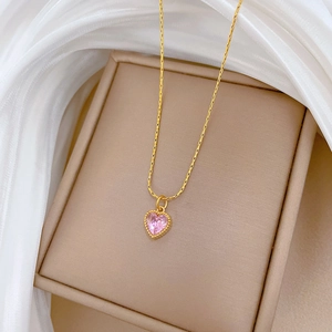 Detail of a gold stainless steel necklace with a pink heart pendant on a jewelry box